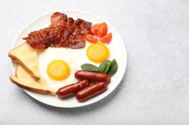 Delicious breakfast with fried eggs, sausages and bacon served on light grey table, closeup. Space for text