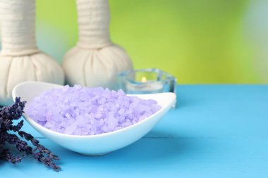 Mor deniz tuzu kasede, bitkisel torbalar ve lavanta çiçekleri açık mavi ahşap masada bulanık yeşil arka planda, yakın plan. Metin için boşluk