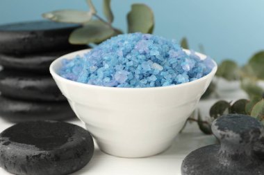 Mavi deniz tuzu kasede, taşlar ve okaliptüs yaprakları beyaz ahşap masada, yakın plan.