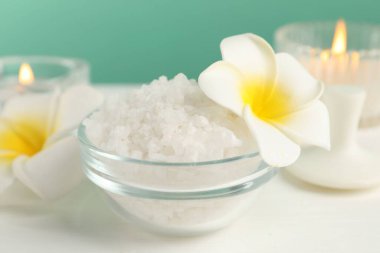 Kasedeki deniz tuzu, yanan mumlar ve çiçekler beyaz ahşap masada turkuaz arka planda, yakın plan