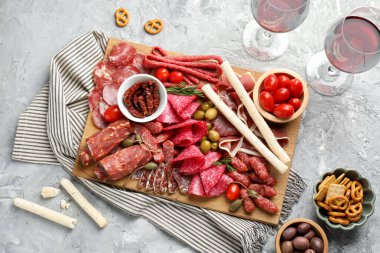 Şarküteri tahtası, farklı pişirilmiş et, sosis ve şarap gri masada, düz yatıyordu.