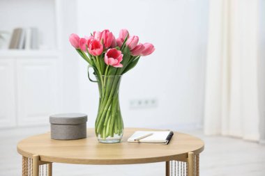 Vazoda pembe lale buketi, not defteri, kalem ve kutu.