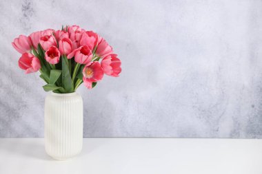 Gri desenli duvarın yanındaki beyaz masadaki vazoda duran pembe lale buketi. Metin için boşluk