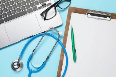 Stetoskop, kalem, dizüstü bilgisayar ve gözlüklü düz mavi arka plan, düz konum