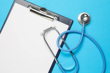 Açık mavi arkaplanda steteskop ve pano, üst görünüm