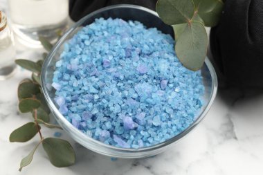 Kasede mavi deniz tuzu, bitkisel torbalar ve beyaz mermer masada okaliptüs dalları, yakın plan.