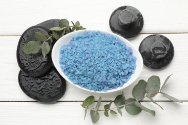 Mavi deniz tuzu kasede, masaj taşları ve okaliptüs dalları beyaz ahşap masada, düz yatıyordu.