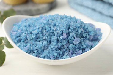 Kasedeki mavi deniz tuzu, havlular ve okaliptüs dalları beyaz ahşap masada, yakın plan.