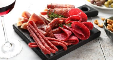 Şarküteri tahtası, farklı pişirilmiş et, sosis ve şarap beyaz fayanslı masada, yakın plan.