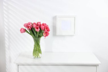Beyaz duvarın yanındaki çekmece çekmecesinde vazoda duran pembe laleler. Metin için boşluk
