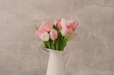 Gri duvarda sürahi içinde güzel laleler.