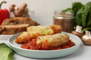 Lezzetli lahana dürümleri ve malzemeler beyaz döşemeli masada, yakın plan.