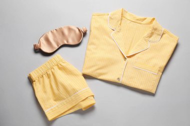 Modaya uygun sarı pijamalar ve açık gri arka planda uyku maskesi.