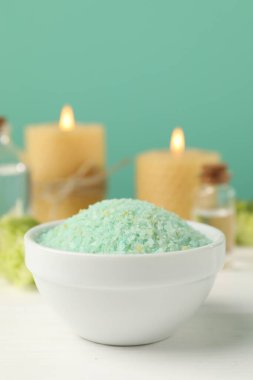 Yeşil deniz tuzu kasede ve yanan mumlar beyaz ahşap masada turkuaz arka planda, yakın plan