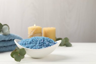 Kasede mavi deniz tuzu, yanan mumlar, havlular ve okaliptüs dalları beyaz ahşap masada, yakın plan. Metin için boşluk