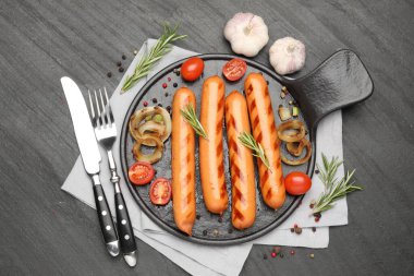 Izgara sosis, domates ve baharatlar siyah masada, düz yerde.