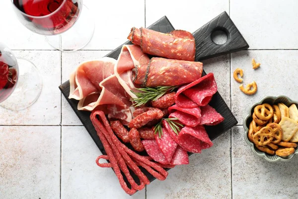 Şarküteri tahtası, farklı pişirilmiş et, sosis ve beyaz fayanslı masa üzerinde şarap.