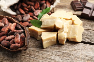 Organik kakao yağı, fasulye ve yeşil yapraklar ahşap masada, yakın plan.