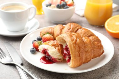 Nefis bir kahvaltı. Reçelli lezzetli kruvasanlar, açık gri masada böğürtlen ve içecekler, yakın plan.