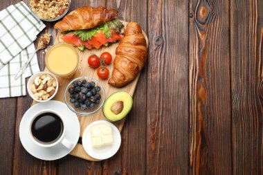 Sağlıklı kahvaltı. Somon, avokado, böğürtlen ve ahşap masada içeceklerle lezzetli kruvasanlar. Metin için boşluk