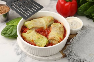 Lezzetli lahana ruloları kasede, malzemeler ve spatula açık mermer masada, yakın plan.