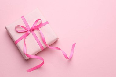 Açık pembe arka planda fiyonklu paketlenmiş hediye, üst manzara. Metin için boşluk