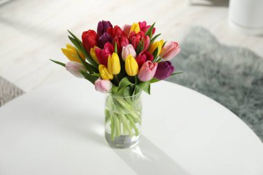 Beyaz masadaki vazoda renkli lalelerden oluşan güzel bir buket.