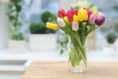 İçerideki ahşap masada vazodaki renkli lalelerden oluşan bir buket. Metin için boşluk