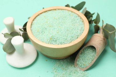 Kase içinde yeşil deniz tuzu, kepçe, masaj taşları ve turkuaz üzerinde okaliptüs dalları, yakın çekim.