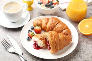 Nefis bir kahvaltı. Reçelli lezzetli kruvasanlar, açık gri masada böğürtlen ve içecekler, yakın plan.