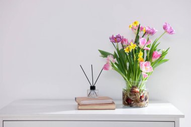 Vazoda güzel bahar çiçekleri, kitaplar ve sazlıklar pencerenin yanındaki şifoniyerde, metin için boşluk