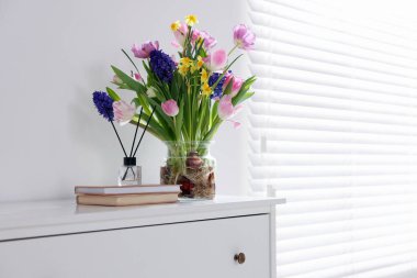 Vazoda güzel bahar çiçekleri, kitaplar ve sazlıklar pencerenin yanındaki şifoniyerde, metin için boşluk