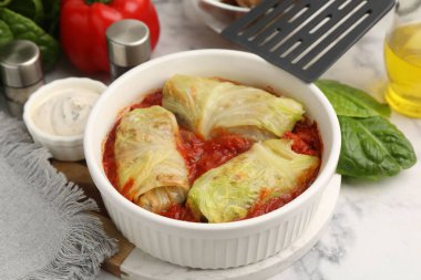 Lezzetli lahana ruloları kasede, malzemeler ve spatula açık mermer masada, yakın plan.