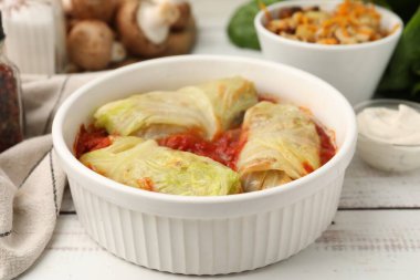 Lezzetli doldurulmuş lahana ruloları kasede ve malzemeler açık ahşap masada, yakın plan.