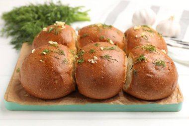 Sarımsaklı taze çörekler ve beyaz ahşap masada dereotlar, yakın plan.