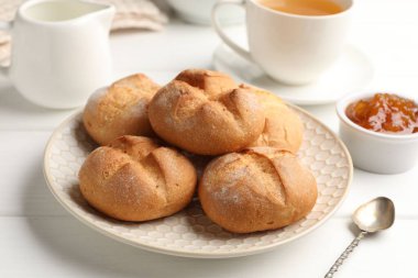 Fresh buns, jam and tea on white wooden table, closeup