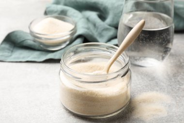 Gelatin powder and glass of water on light grey table, closeup