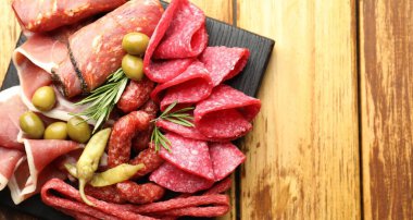 Şarküteri tahtası, farklı pişmiş et, sosis ve ahşap masa üzerinde zeytin, üst manzara. Metin için boşluk