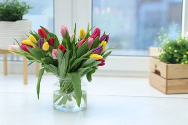 Beyaz masadaki vazodaki renkli lalelerden oluşan güzel bir buket. Metin için boşluk