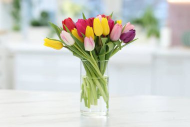 Beyaz masadaki vazoda renkli lalelerden oluşan güzel bir buket.