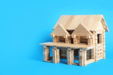 Açık mavi arka planda tahta bloklardan yapılmış bir ev. Metin için boşluk