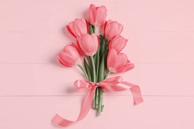 Pembe ahşap masa üzerinde kurdeleli güzel laleler.