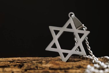 Soykırım Anma Günü. Davut Yıldızı şeklindeki kolye ve tahta yüzeyde siyah arka planda metal zincir, yakın plan. Metin için boşluk