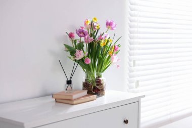 Vazoda güzel bahar çiçekleri, kitaplar ve sazlıklar pencerenin yanındaki şifoniyerde, metin için boşluk