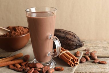 Cam bardakta nefis kakao, fasulye, pudra ve tarçın çubukları bej arka planda, yakın plan. Metin için boşluk