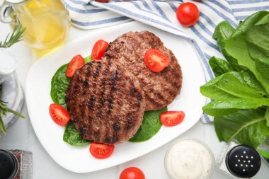 Lezzetli ızgara et köfteleri, domatesler ve beyaz fayanslı masada ıspanak.