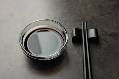 Soya sosu cam kasede ve çubuklar gri masada, yakın plan.