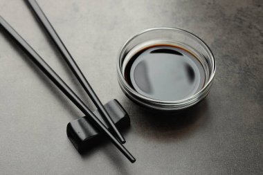 Soya sosu cam kasede ve çubuklar gri masada, yakın plan.