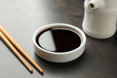 Soya sosu kasede ve çubuklar gri masada, yakın plan.