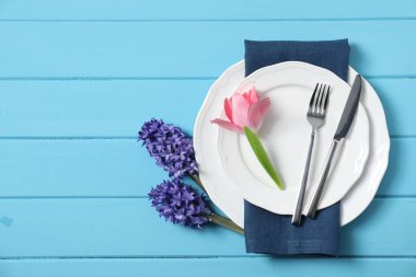 Stylish table setting with floral decor on light blue wooden background, flat lay. Space for text